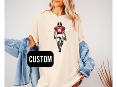 This football shirt is a great gift for any football fan that wants to show off their favorite player..  ✨Shipping & Processing - Please allow 2-5 business days for your item to be processed and printed. Processing times may be longer during busy holiday periods. - Your order ships from the US. Allow 2-7 business days shipping. Unfortunately, I am unable to guarantee USPS shipping times. ✨Returns✨ If there is a defect with your order, please reach out to us within 15 days of receiving the item. Collegiate T-shirt With Custom Print For Game Day, Varsity T-shirt For College Football Season, Customizable T-shirt For Football Season, Sporty T-shirt For Game Day During Football Season, Sports Fan T-shirt For Football Season, Custom Print Crew Neck T-shirt For Game Day, Customizable Casual T-shirt For Football Season, Varsity Football Season Fan Gear T-shirt, Varsity T-shirt With Custom Print For Game Day