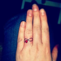 a woman's hand with a small bow tattoo on her left ring, and a red heart in the middle