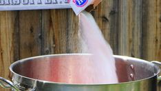 a person pouring water into a large metal pot on the side of a wooden fence