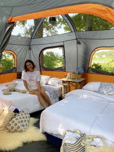 a woman sitting on top of a bed in a tent next to two twin beds