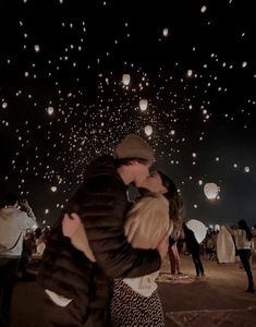 a man and woman kissing in front of many lit up paper lanterns at night time