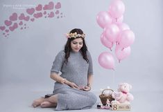 a woman sitting on the ground with balloons and a teddy bear in front of her