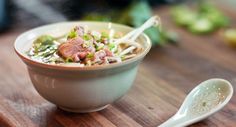 a bowl of soup with meat and vegetables on a wooden table next to a spoon