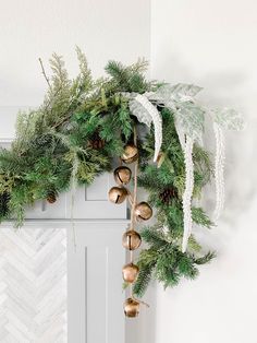 a christmas wreath with gold bells and greenery hanging from the front of a white door