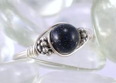 "Blue Goldstone and Bali Sterling Silver Wire Wrapped Ring This ring is handcrafted with a 6 mm Blue Goldstone and two bali sterling silver beads on sterling silver wire. This is a representation of the exact ring you will receive. With being real gemstones, there are variations in all gems, so please keep that in mind. This ring can be made for any size from 2 to 15 including half sizes. These rings can not be resized after they are made. The picture is enlarged to show detail. Ring Size: Pleas Blue Sterling Silver Wire Wrapped Rings, Wire Wrapped Ring, Blue Goldstone, Sterling Silver Wire Wrap, All Gems, Wire Wrapped Rings, Beaded Rings, Sterling Silver Bead, Silver Wire