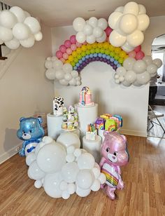 a room filled with balloons and stuffed animals on the floor next to a rainbow arch