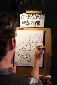 a man is drawing on a whiteboard in front of a microphone and sign that reads caricatures drawn by 11 pm