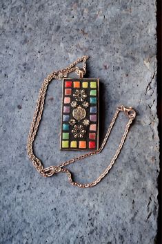 a multicolored necklace with a chain attached to it sitting on a stone surface