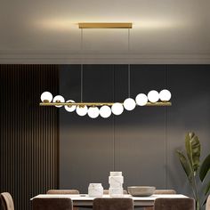 a dining room table and chairs with lights hanging from the ceiling above it, in front of a black wall