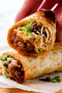 a hand holding a burrito filled with meat and veggies on top of it