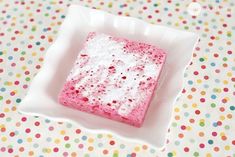 a small square cake in a white plate on a polka dot tablecloth with colorful dots