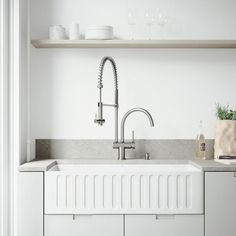 a kitchen with white cabinets and countertops has a sink, faucet, and shelving