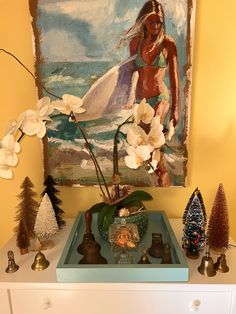 a painting is on the wall above a dresser with christmas trees and ornaments in front of it