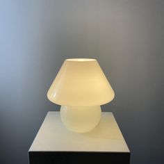 a white table lamp sitting on top of a wooden block in front of a gray wall