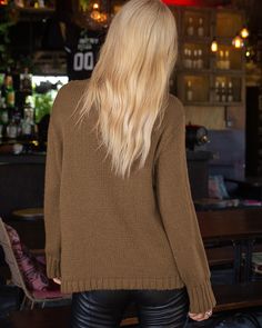 the back of a woman wearing black leather pants and a brown sweater in a bar