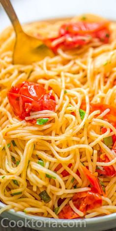 a close up of a bowl of spaghetti with tomatoes and green peppers on top, with a spoon in it