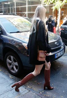 a woman is walking down the street with her handbag in her pocket and boots on