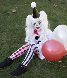 a clown sitting in the grass with balloons