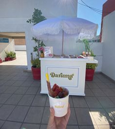 a person holding up a paper cup with fruit in front of an ice cream stand