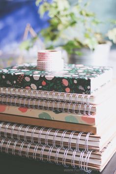 a stack of notebooks sitting on top of a table next to a potted plant