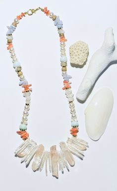 an assortment of sea shells and seashells displayed on a white surface with a gold - tone bead necklace