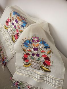 two white scarves with colorful designs on them sitting on a table next to each other