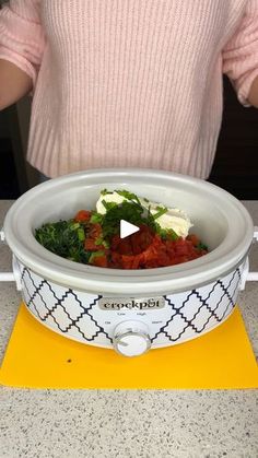 a woman holding a bowl with vegetables in it on top of a yellow table mat