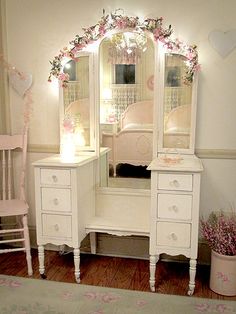 a bedroom with a white dresser, mirror and pink bed in the corner is lit up by fairy lights