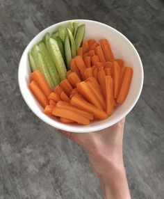 a person holding a bowl full of carrots and cucumber slices in it