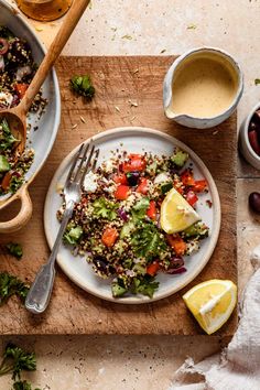 a plate of salad with lemons and olives next to some dipping sauce on a cutting board