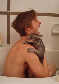 a man holding a cat while sitting in a bathtub with his back turned to the side