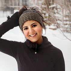 a woman is smiling while wearing a black jacket and a knitted headband in the snow