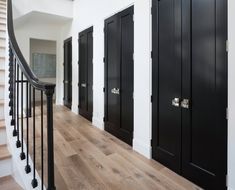 an entry way with black doors and wooden floors, along with banisters that lead up to the second floor