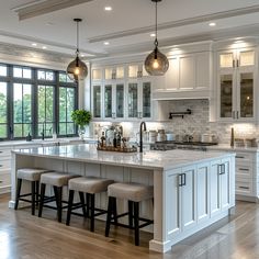 a large kitchen with white cabinets and marble counter tops, an island with four stools