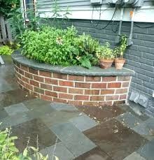 a brick planter with potted plants on the side of it and an umbrella in the background