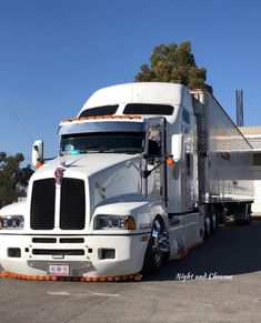 a white semi truck parked in a parking lot next to a trailer house and trees