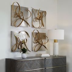 three metal art pieces mounted on the wall above a dresser with a lamp and vase