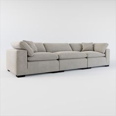 a long couch with pillows on it in front of a white wall and grey floor