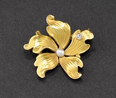 Offered is a beautiful, dainty and petite Art Nouveau period gold flower brooch pin in lovely original condition. Finely made in 14K yellow gold, the piece retains most of its original bloomed finish with the characteristic matte surface so popular at the time.  At its center rests a lustrous creamy pearl, and a tiny but fiery old mine cut diamond sparkles like a spot of dew on one petal. The small size of this pretty pin makes it quite versatile.  It measures approximately 7/8 of an inch in dia Gold Flower Brooch For Formal Occasions, Yellow Gold Flower Brooch Jewelry, Formal Flower Shaped Hallmarked Brooch, Yellow Gold Flower Brooch, Elegant Gold Flower Brooch, Elegant Gold Flower Brooches, Old Mine Cut Diamond, Pretty Pins, Antique Pendant