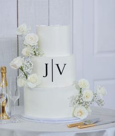 a wedding cake with white flowers and the initials jlv on it next to a bottle of champagne