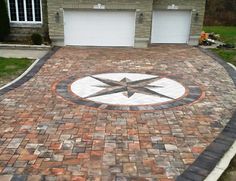 a brick driveway with a compass design on the side and two garages behind it