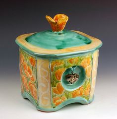 a ceramic box with an orange flower on top and a bee in the center sitting inside it