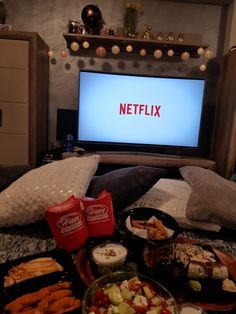 a television sitting on top of a bed next to a pile of food and drinks