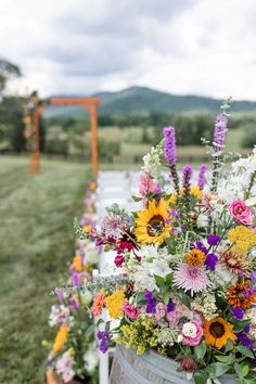 a bucket filled with lots of flowers sitting on top of a grass covered field next to a wooden bench