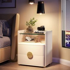 a night stand with a book, lamp and pictures on it in front of a bed