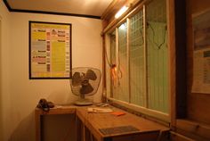 a fan sitting on top of a wooden table in front of a wall mounted poster