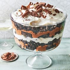 a trifle with whipped cream and chocolate toppings in a glass dish next to two wine glasses