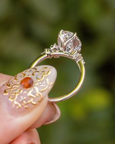 a woman's hand holding a gold and white ring with an orange stone on it