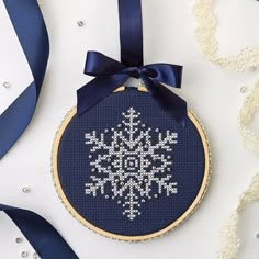 a cross stitch snowflake ornament hanging from a blue ribbon on a white background