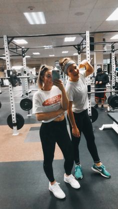 two women are taking a selfie in the gym with their cell phones while standing next to each other